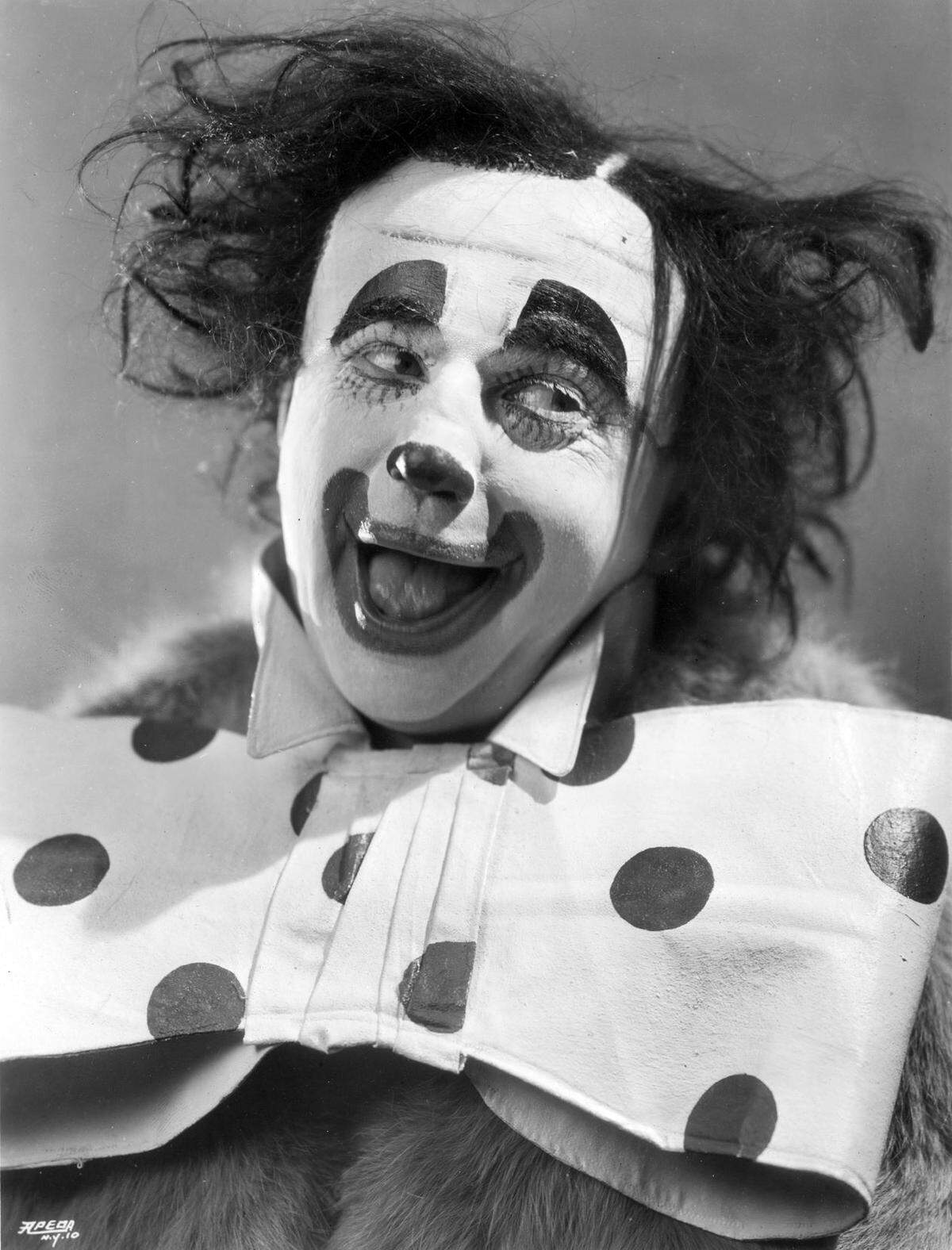A clown smiles in a portrait wearing an oversized polka-dot bow tie.