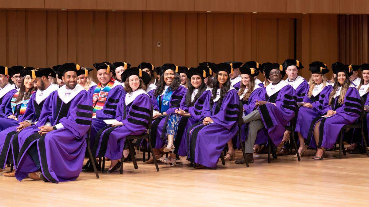 Students in purple gowns seated in rows during hooding ceremony.