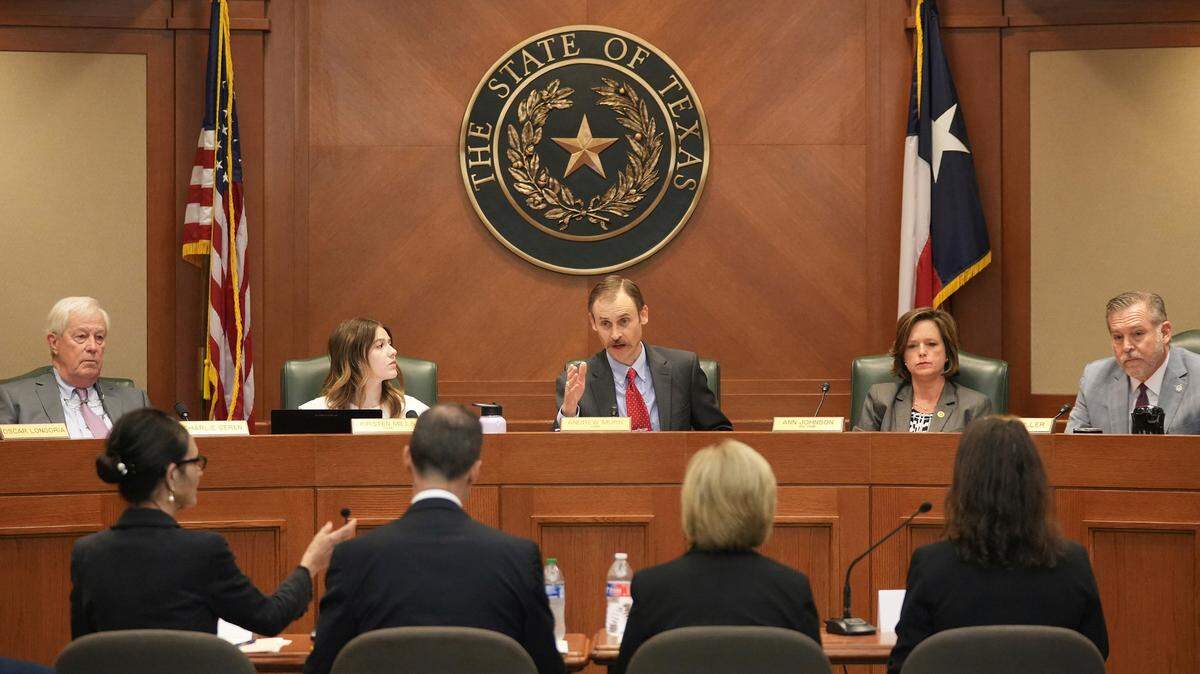 A man in a blue suit sits behind a desk under a seal of the state of Texas during a House committee hearing.