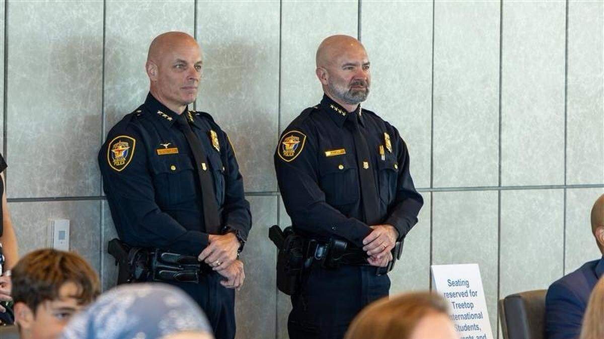 Two bald white police commanders standing up against a wall