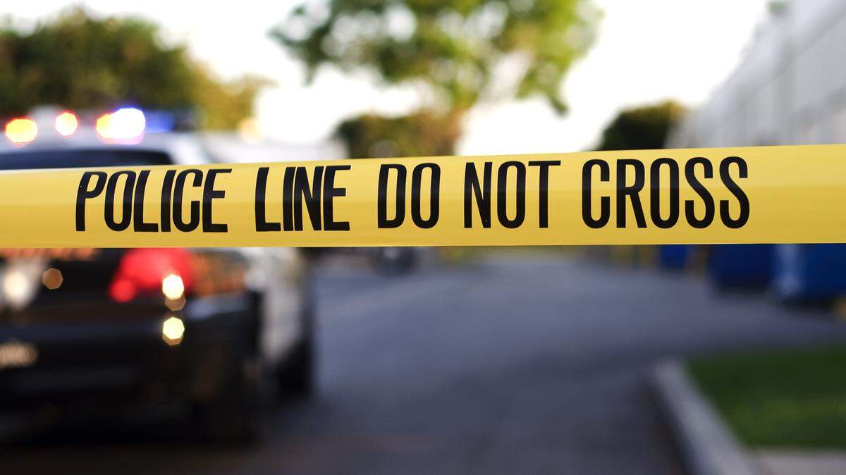 A blurred police car in the background behind yellow crime scene tape.