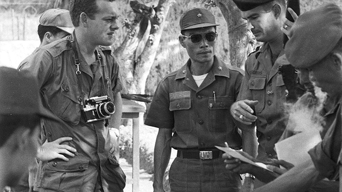 Fort Worth Star-Telegram reporter Bob Schieffer, left, speaking with U.S. Army Lieutenant Donald W. Harris of College Station, Texas, right, who was in charge of supervising distribution of food to dependents of Vietnamese villagers who come to the regional defense training center, located in Coa Long of the Kien Phong Province of South Vietnam, to learn how to defend their homes from the Viet Cong during the Vietnam War. Shown with Harris is his Vietnamese counterpart, Lieutenant Be, center.