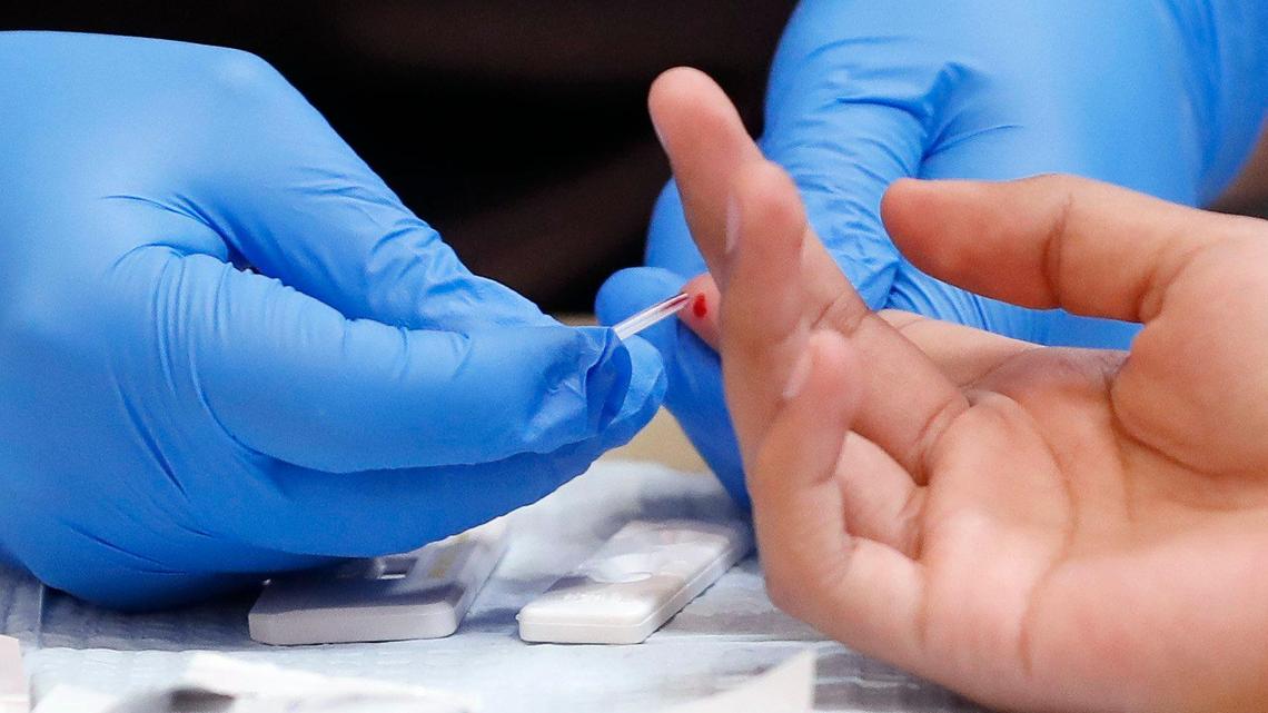 A closeup photo of hands in blue gloves taking a blood sample from a small droplet on a second persons finger.