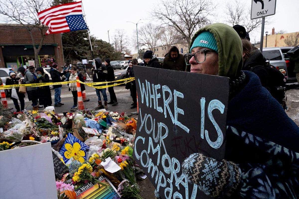 A woman holds a sign while visiting the makeshift memorial in the area where Alex Pretti was shot and killed by Federal immigration agents in Minneapolis, Minnesota, on January 26, 2026. On January 24, federal agents shot and killed Alex Pretti, a 37-year-old ICU nurse, while scuffling with him on an icy roadway in Minneapolis, less than three weeks after an immigration officer fired on Renee Good, also 37, killing her in her car. US President Donald Trump blamed their deaths on Democratic "chaos," as his administration faced intensifying pressure over its mass immigration crackdown in Minneapolis. (Photo by ROBERTO SCHMIDT / AFP via Getty Images)