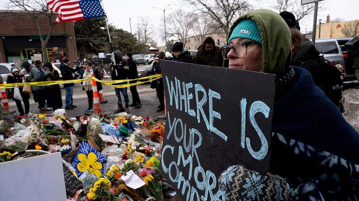 A woman holds a sign while visiting the makeshift memorial in the area where Alex Pretti was shot and killed by Federal immigration agents in Minneapolis, Minnesota, on January 26, 2026. On January 24, federal agents shot and killed Alex Pretti, a 37-year-old ICU nurse, while scuffling with him on an icy roadway in Minneapolis, less than three weeks after an immigration officer fired on Renee Good, also 37, killing her in her car. US President Donald Trump blamed their deaths on Democratic "chaos," as his administration faced intensifying pressure over its mass immigration crackdown in Minneapolis. (Photo by ROBERTO SCHMIDT / AFP via Getty Images)