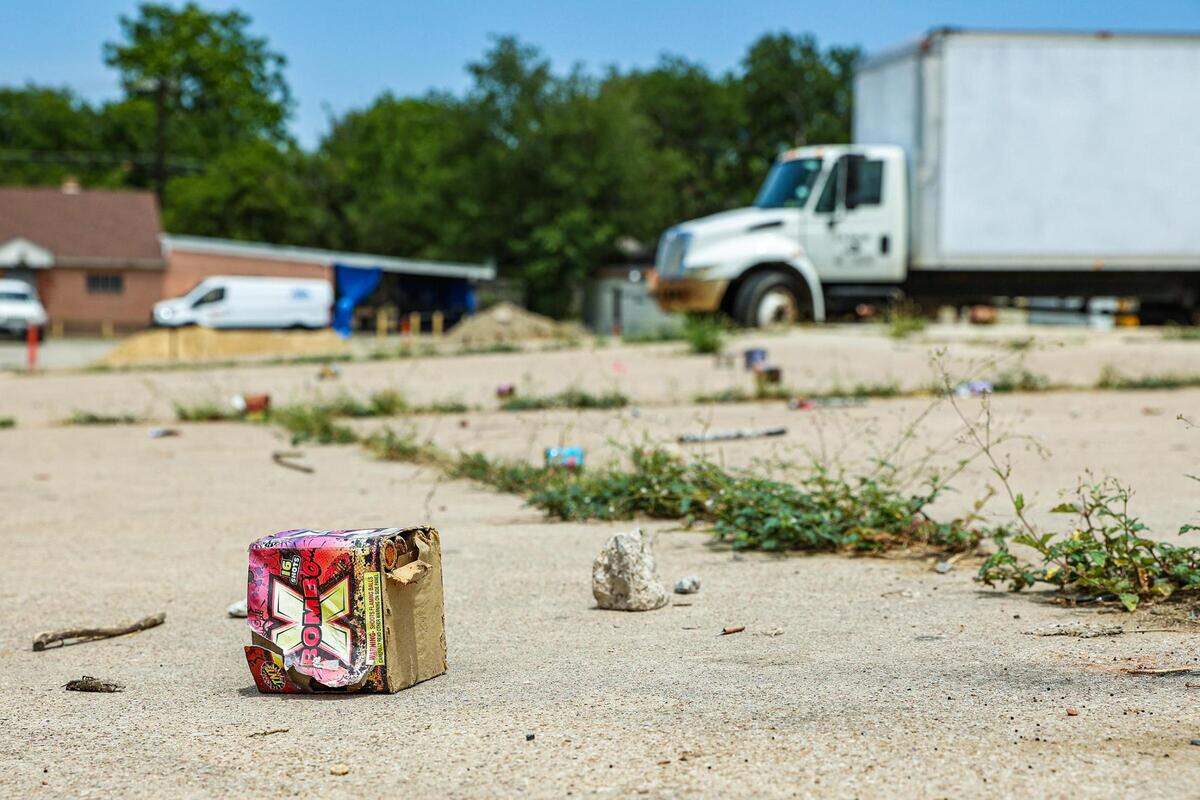 A fireworks box along with other trash is scattered on a slab of concrete, empty besides a large white truck pared to the right.