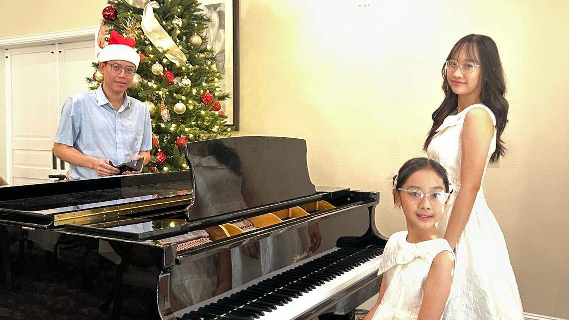 Sisters My, 10, and Linh Phan, 16, are using their piano talents to bring joy to seniors in nursing homes. In the background, wearing a Santa hat as part of a Christmas concert, is their father Vinh Phan.