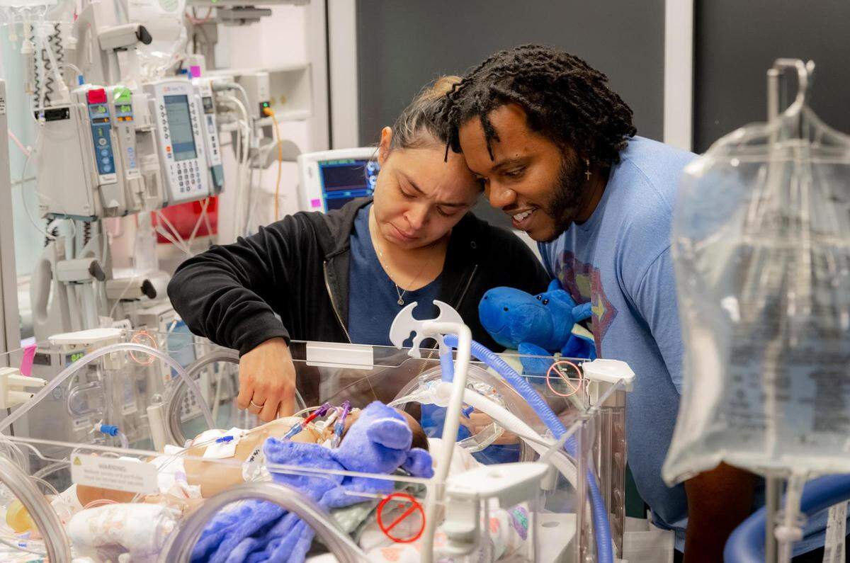 The couple is smiling over their babies in a hospital room. 