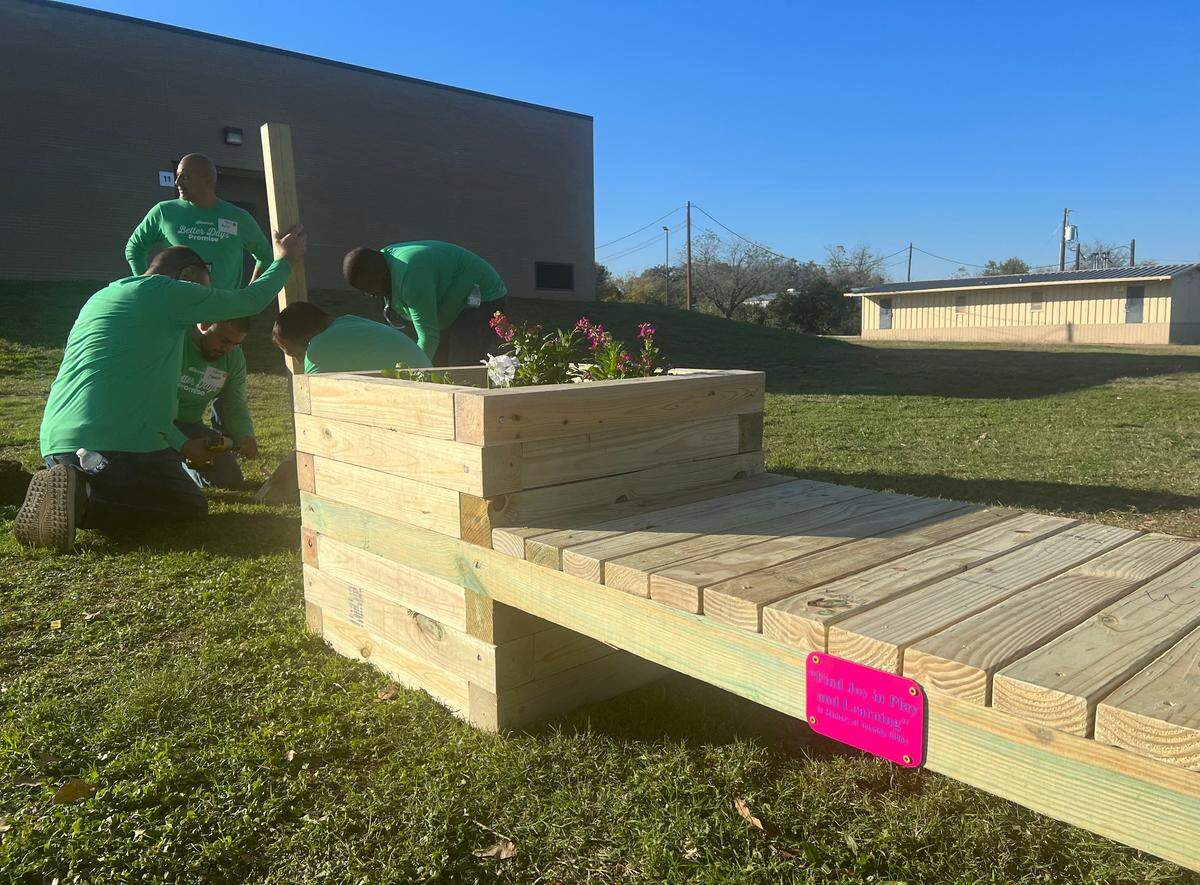 Kellanova employees install a post for a miniature library on Tuesday, Nov. 14, 2023, next to a bench dedicated to Yolanda Gibbs, a cafeteria worker at David K. Sellars Elementary School who was fatally shot outside of the school on Oct. 11. The bench was built alongside a new playground.