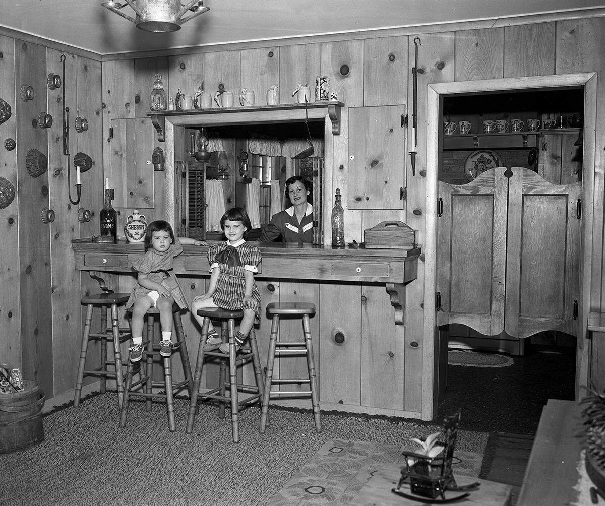May 6, 1953: Looking toward the bar and kitchen from the Campbell living room. Mrs. Campbell, and her daughters Melissa and Melinda, sitting on bar stools.
