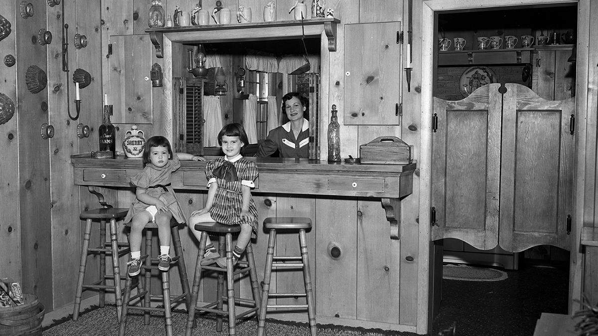 May 6, 1953: Looking toward the bar and kitchen from the Campbell living room. Mrs. Campbell, and her daughters Melissa and Melinda, sitting on bar stools.