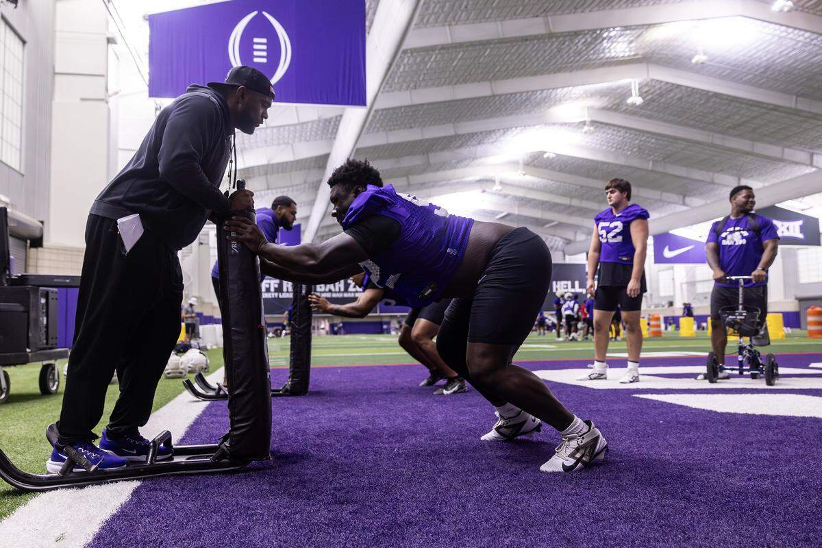 A coach stands on a football sled, left, while Ansel Din-Mbuh pushes the sled.