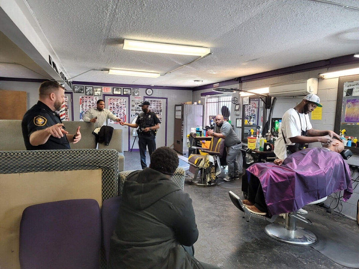 One barber cuts a client's hair while officers stand around them in conversation. 