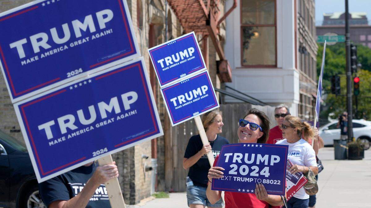 Trump supporters walk with signs near Fiserv Forum as work is done Tuesday in preparation for the Aug. 23 Republican presidential debate in Milwaukee.