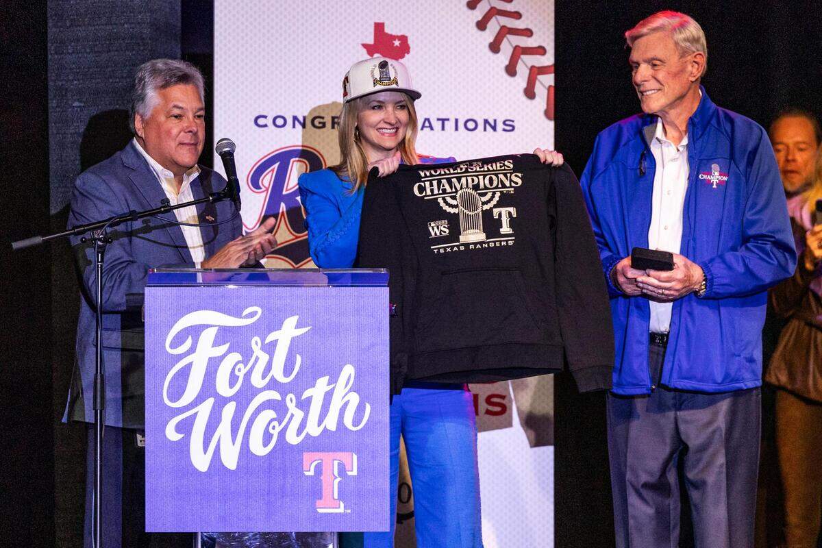 Texas Rangers President Neil Leibman, left, and Owner Ray Davis, right, gift a World Series hat and shirt to Fort Worth Mayor Mattie Parker on her birthday for the World Series celebration event at Billy Bob’s Texas in Fort Worth on Thursday, Nov. 9, 2023.