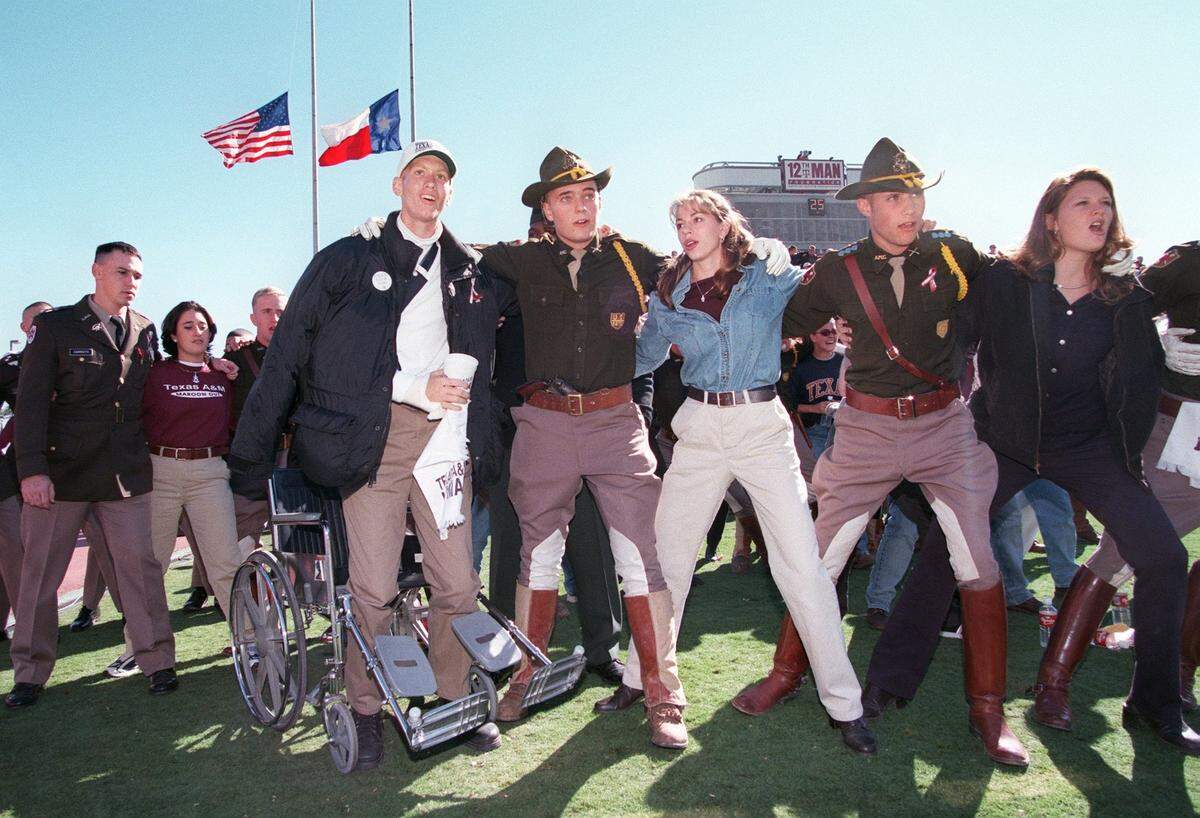 Aggie freshman Dominic Braus of Hallettsville gets out of his wheelchair to lock arms with members of Parson’s Mounted Cavalry and their dates to sing the Aggie War Hymn at the Texas-Texas A&M game in College Station, on Friday, Nov. 26, 1999. Braus suffered injuries to his shoulder, lungs and toes in the collapse of the Aggie bonfire.