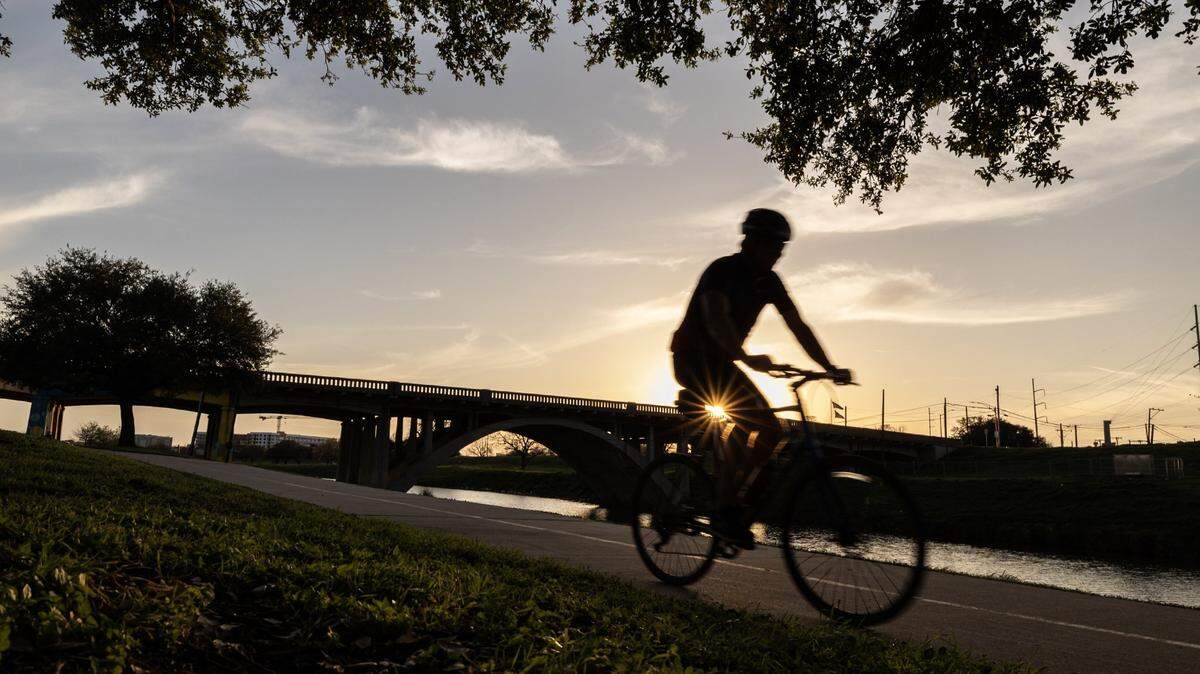 A cyclist biking along a river silhouetted against the setting sun