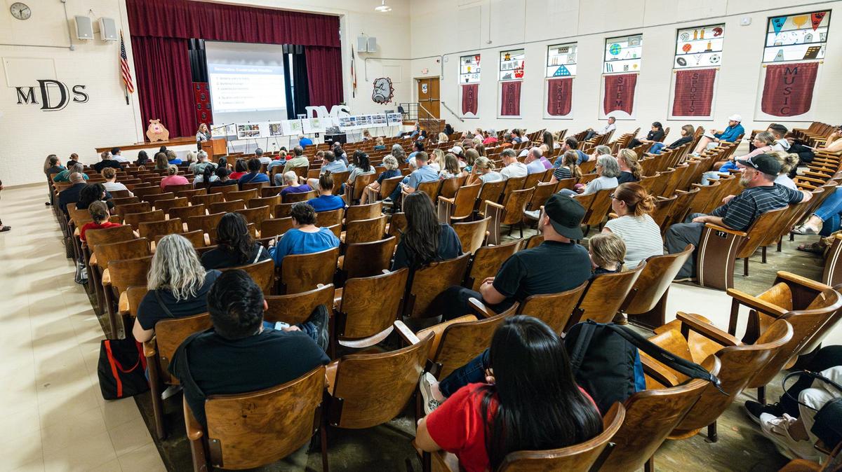 People sit in wooden seats and listen to a speaker talking.