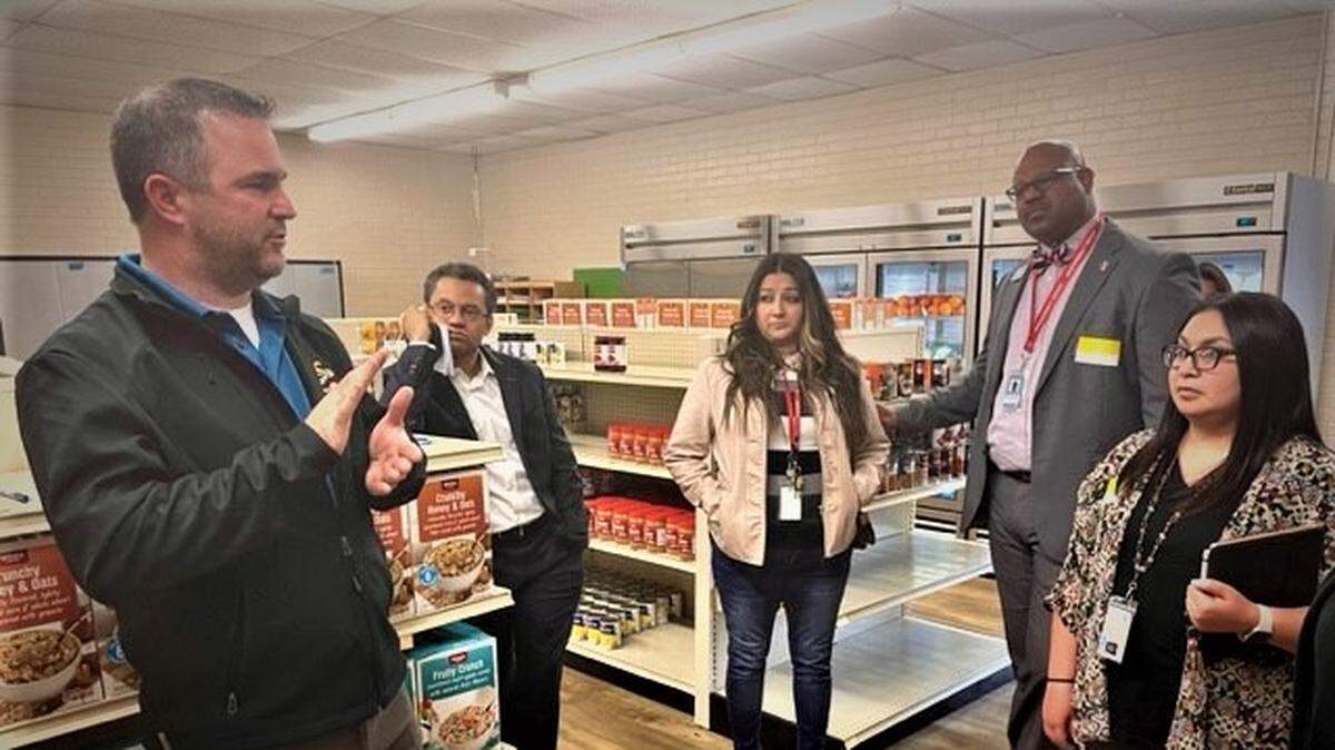 A man in a black fleece pullover talks to four people in a grocery store.