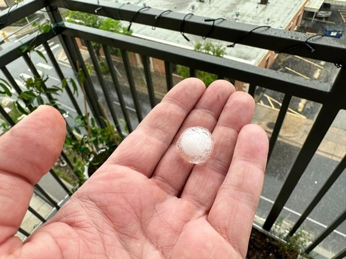 A man's hand holds a small piece of hail while standing on an apartment balcony.