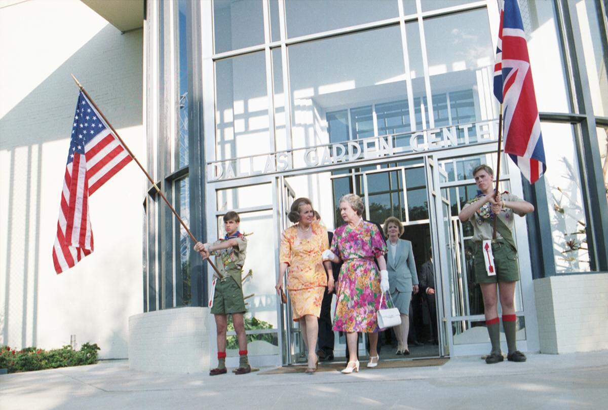 Queen Elizabeth and Dallas Mayor Annette Strauss walk out of the Dallas Garden Center during the Queen’s visit to Dallas on May 21, 1991. Kay Granger, newly elected mayor of Fort Worth, is behind them. Two local boy scouts are seen at the sides of the open doors, one is holding an American flag while the other is holding a British flag.