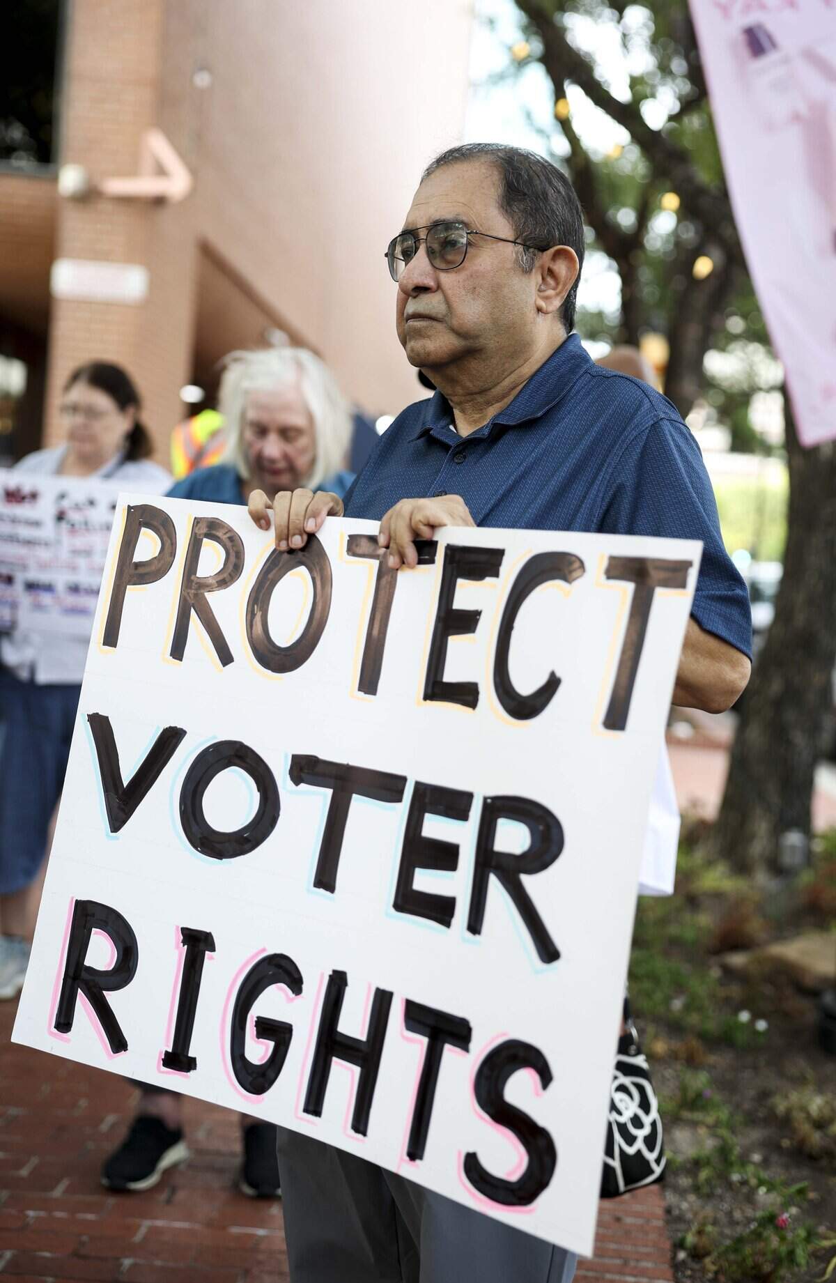 Aftab Siddiqui with the Peace and Justice Center protests outside of the Tarrant County Commissioners Court against the proposed cut of polling places on Tuesday, Aug. 4, 2026 in Fort Worth.