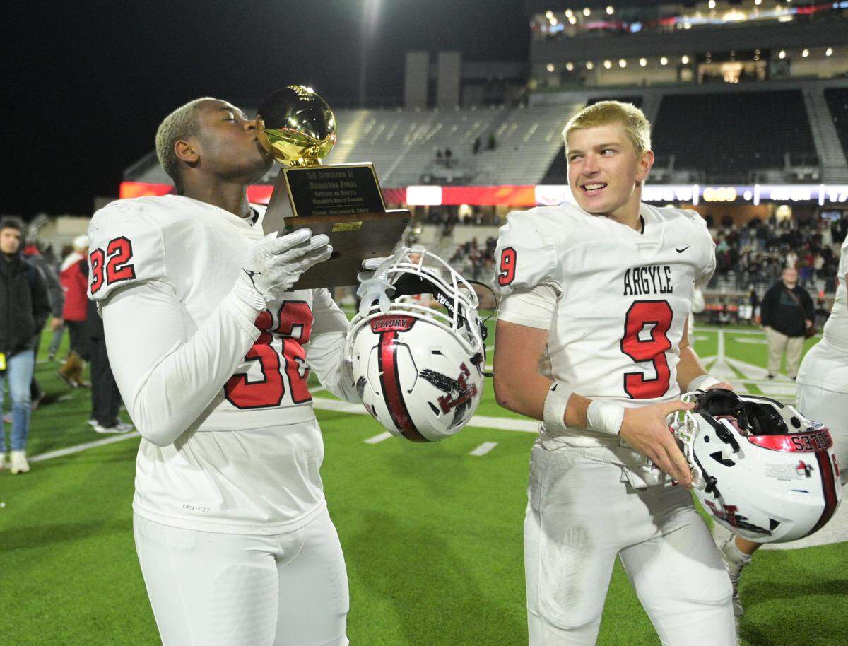 Argyle linebacker Max Bland (32) kisses the 5A Division ll Region l trophy while walking alongside teammate Thomas Irwin (9) after winning the Class 5A Division II Region I playoff game against Lovejoy High School at Prosper ISD Children’s Health Stadium in Prosper, Texas on Friday, Dec. 6, 2024.
