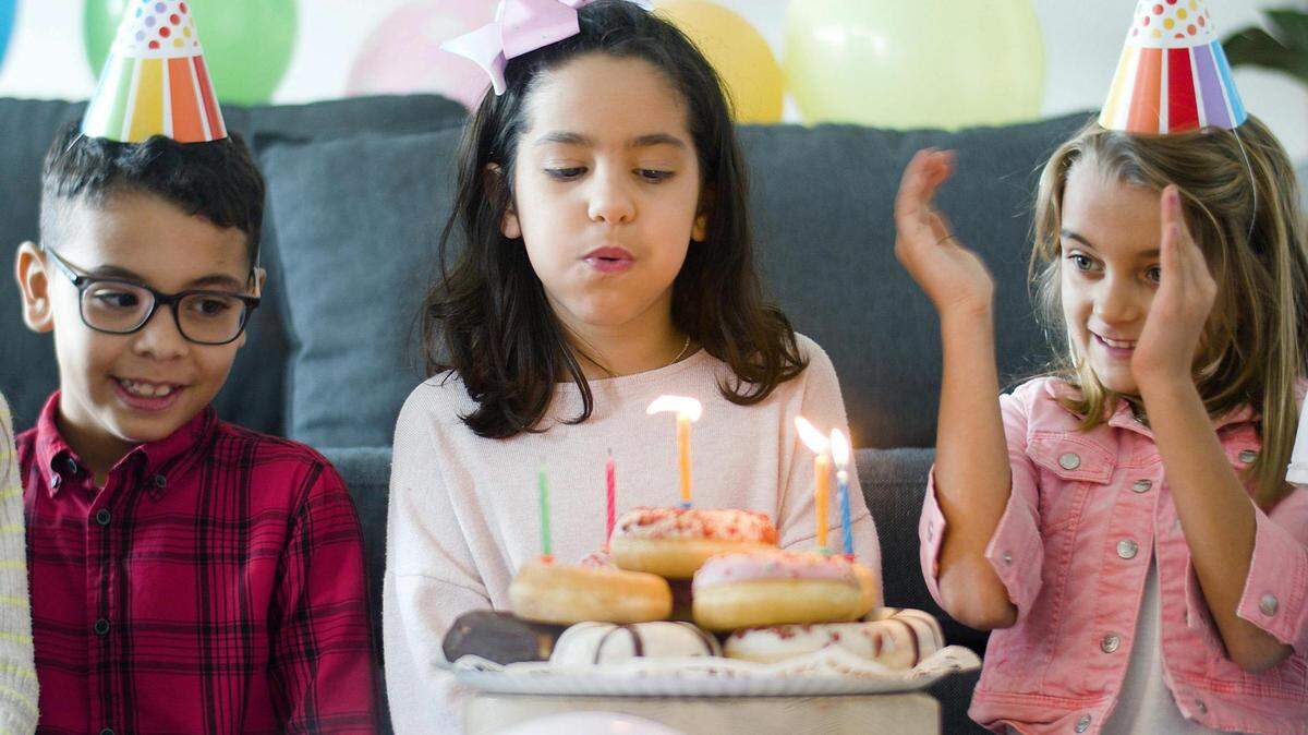 Kids sitting on the floor near a plate of donuts with candles.
