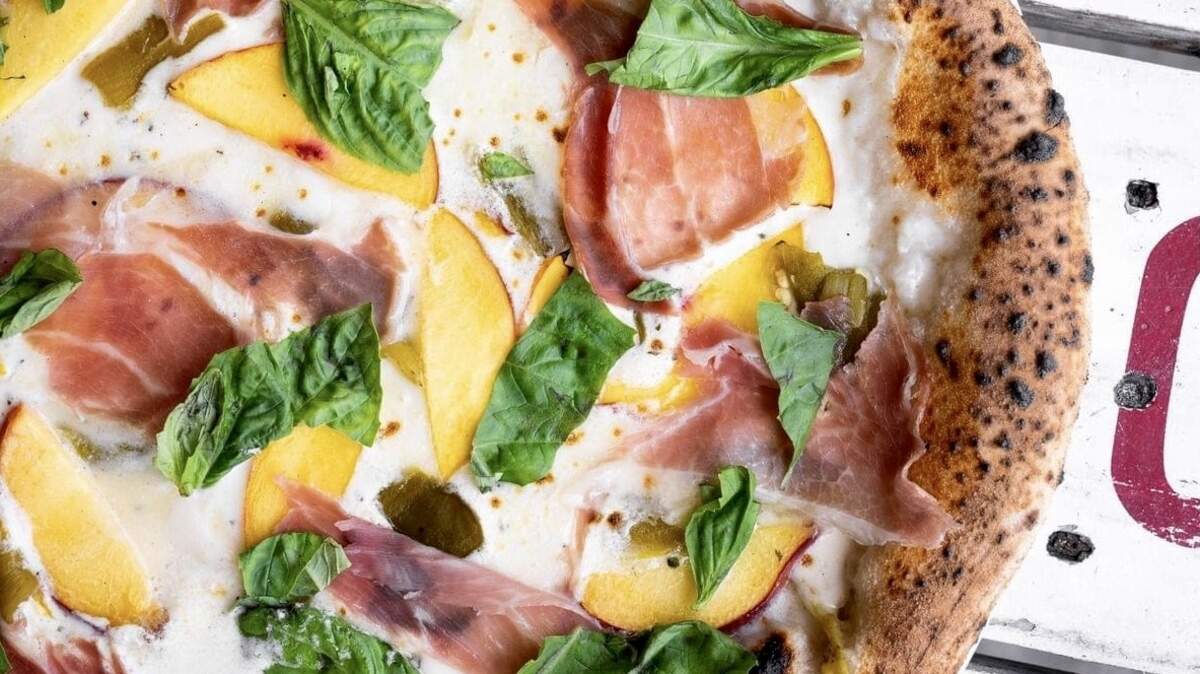 A “peaches and cream” pizza at Cane Rosso features housemade mozzarella, herb mascarpone cheese, roasted Hatch chiles, peaches, prosciutto, and fresh basil.