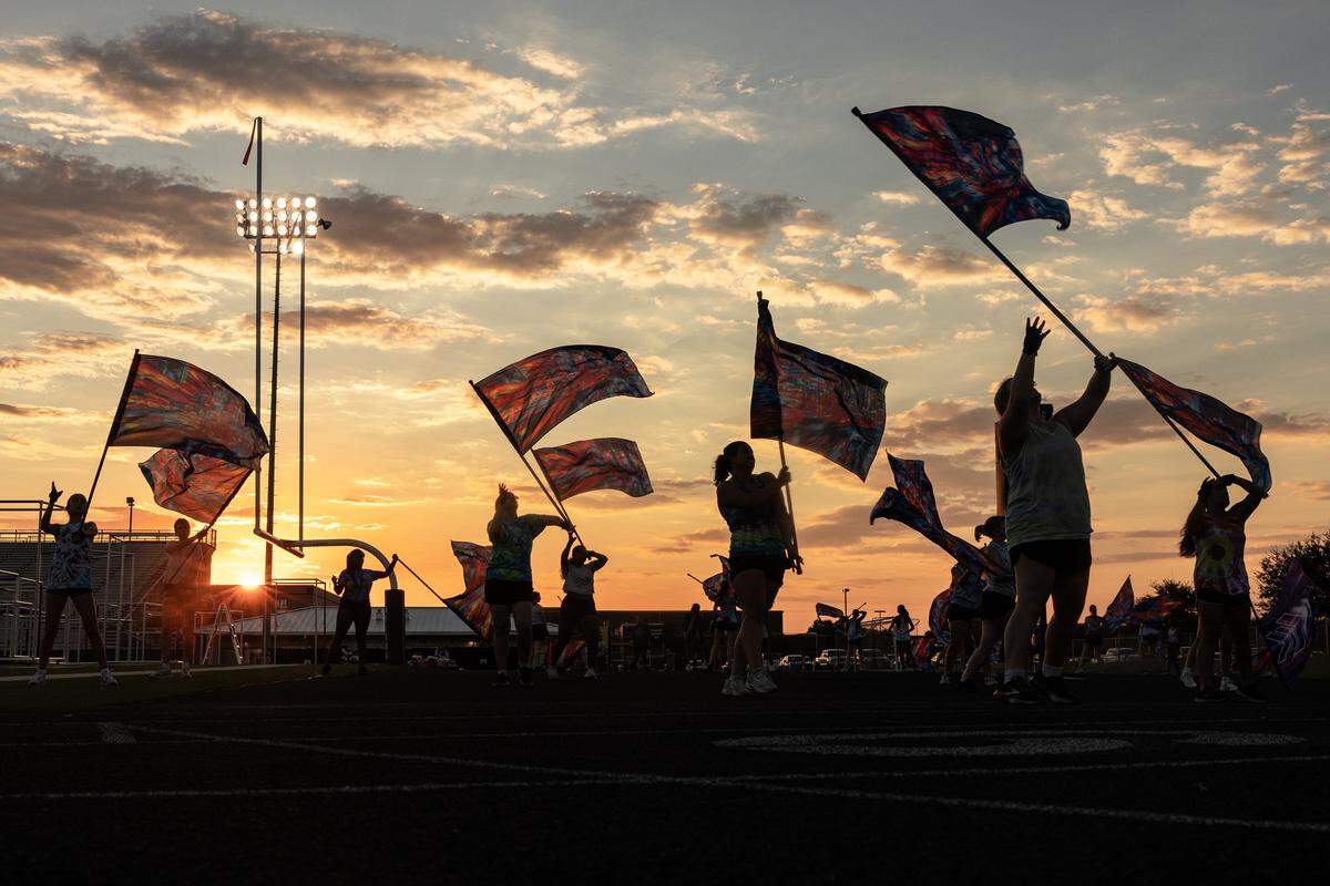 Flags can be seen waving in a vibrant sky lit orange and blue from the sun setting.