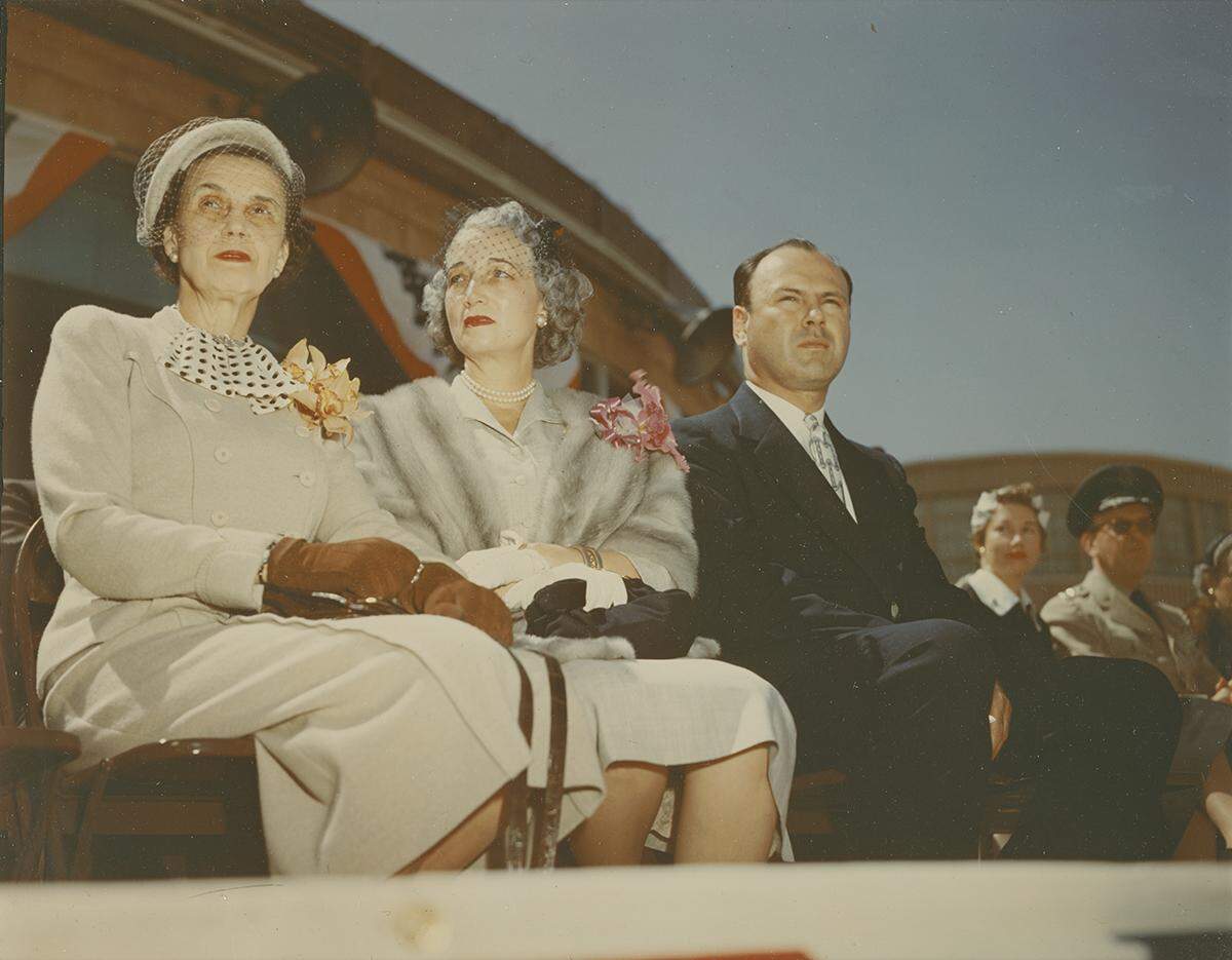 The trio is seated for opening day ceremonies wearing formal dress in this color photograph.
