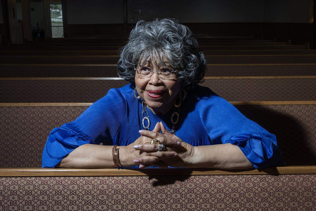 Shirley Benton sits in an aisle of a church, leaning on the pew in front of her.