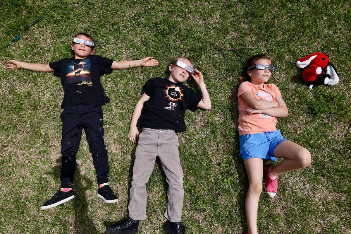 Brothers Nathan, 8 and Dean Dinino, 7, from Washington, lay down with Ada June, 8, to watch the solar eclipse outside the Hill County Courthouse on Monday, April 8, 2024, in Hillsboro.