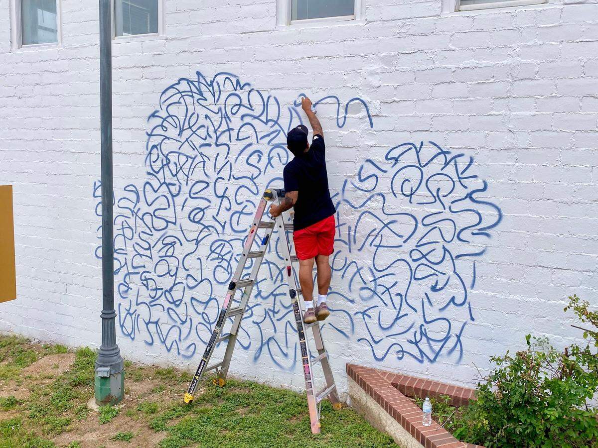 Velasquez is spray painting a doodle grid to help outline the beginnings of the mural.