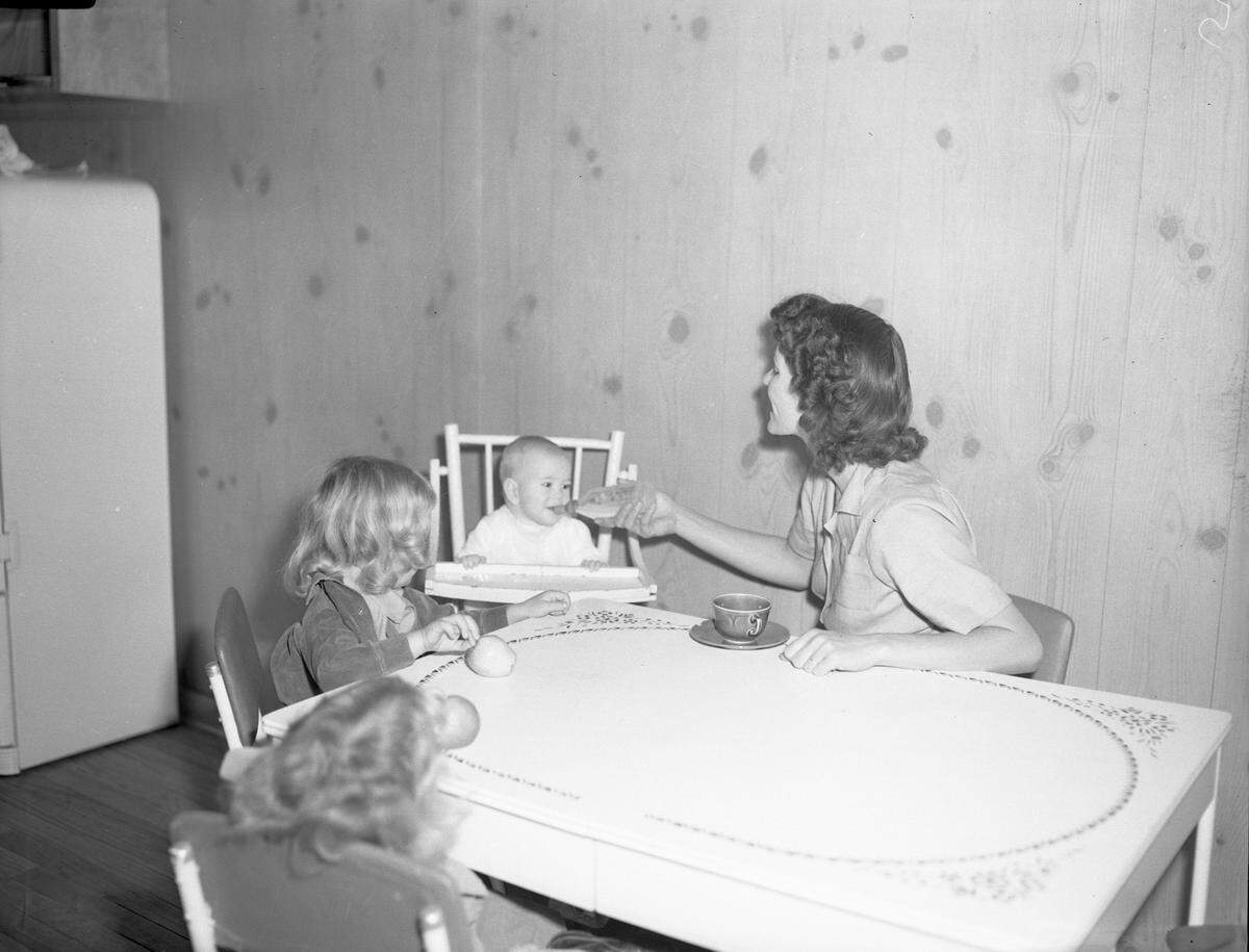 Robin W. “Billie” Mitchell and her three children Robin Carol, Linda, and Stephen enjoy a snack in the kitchen after settling into their new Liberator Village home in February 1943. Child care and schooling through the tenth grade were offered so women could work at the bomber plant.
