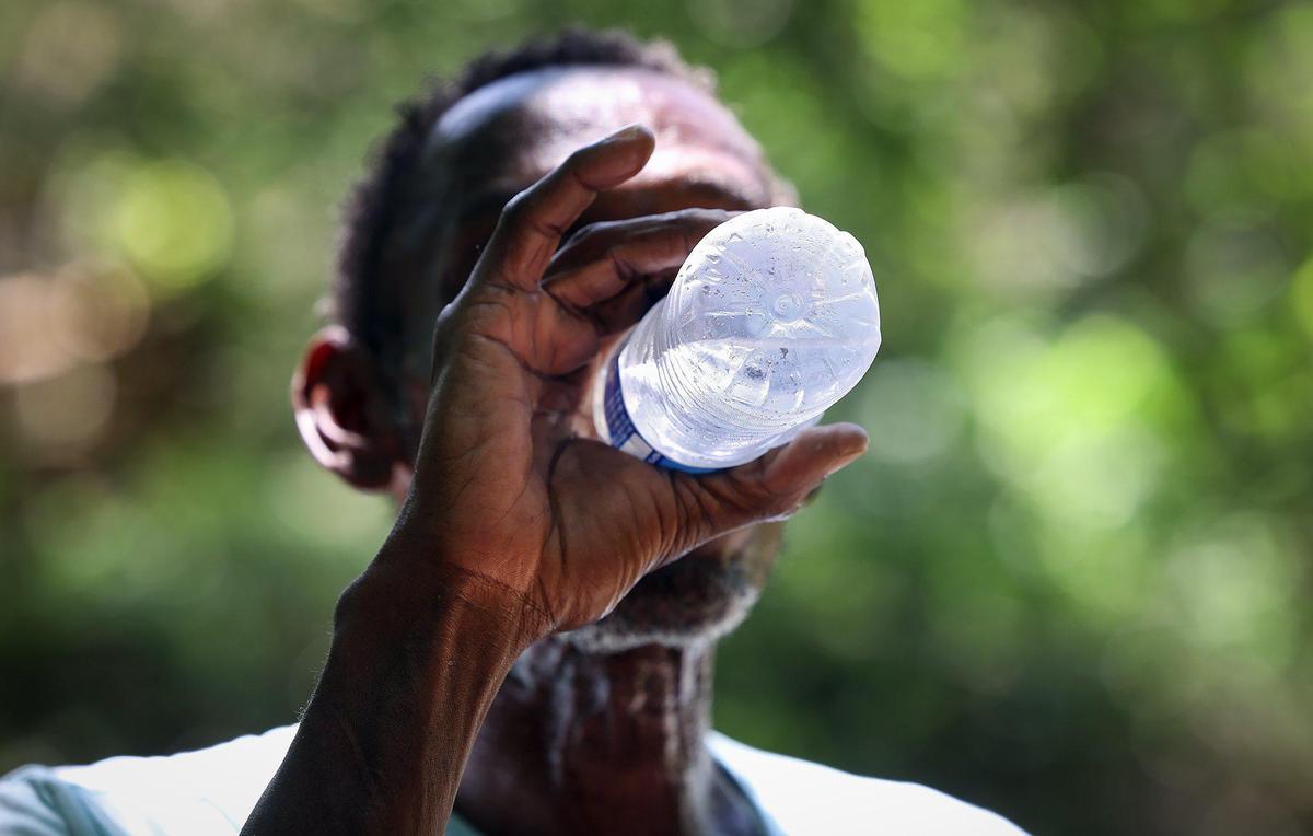 Gary Randle, 61, drinks a bottle of cold water brought by the DRC outreach team while visiting his camp on Friday, June 30, 2023. The nation’s persistent housing crisis coupled with increasingly hot summers has left the most vulnerable, including the unhoused, at particular risk for getting sick from or dying from the heat.