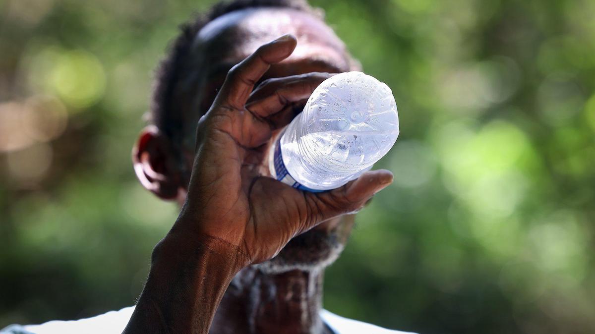 Gary Randle, 61, drinks a bottle of cold water brought by the DRC outreach team while visiting his camp on Friday, June 30, 2023. The nation’s persistent housing crisis coupled with increasingly hot summers has left the most vulnerable, including the unhoused, at particular risk for getting sick from or dying from the heat.