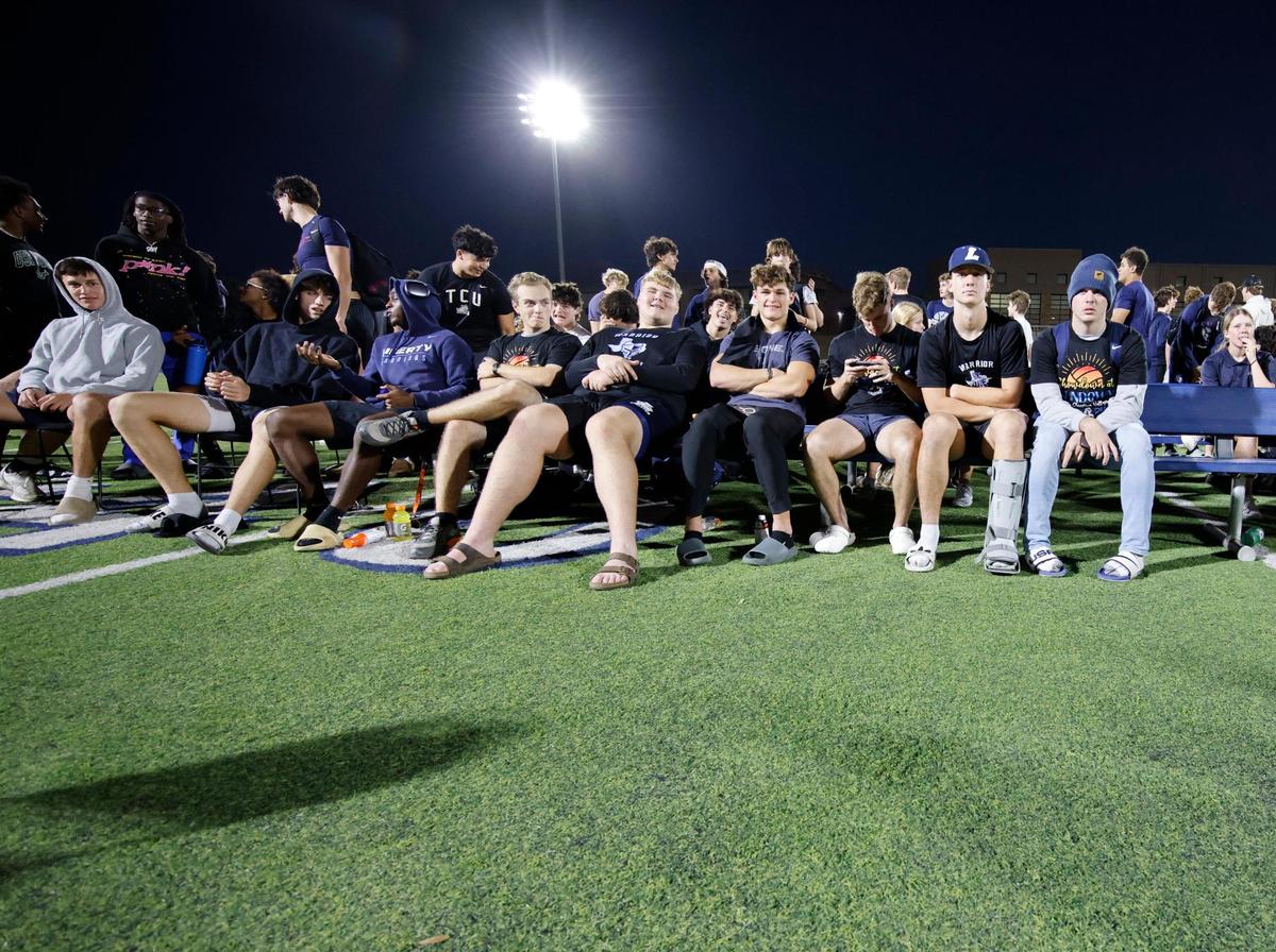 The Warrior football team watches the Showdown at Sundown outdoor exhibition volleyball game from mid field at Liberty Christian High School in Argyle, Texas, Tuesday, Oct. 29, 2024.