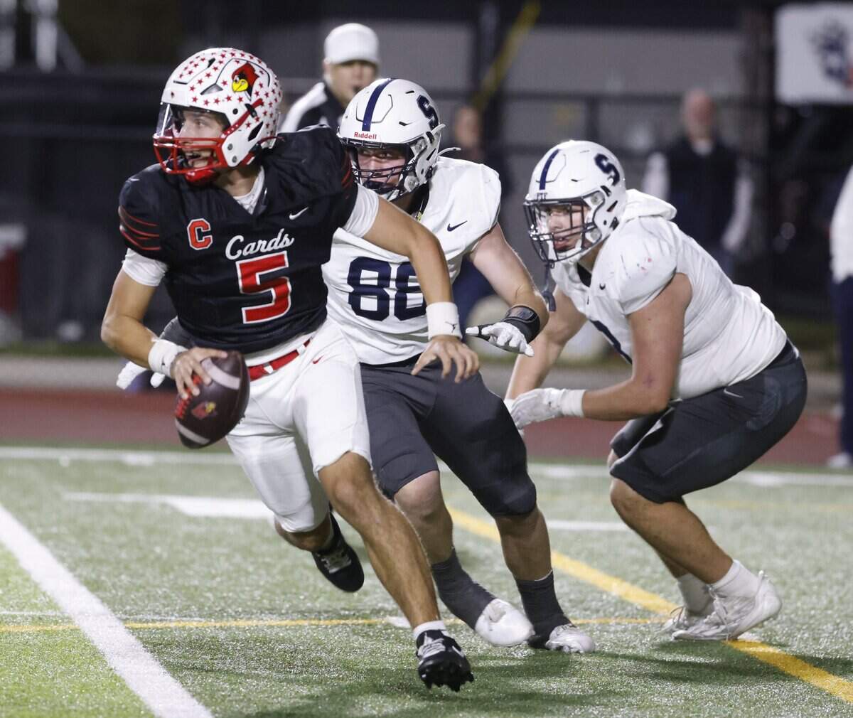 Fort Worth Christian quarterback Landon Gigliotta (5) is pressured out of the pocket by All Saints defensive tackle Kingston Beyer (3) and defensive end Hudson Harbuck (88) during the second half of a TAPPS football game between Fort Worth All Saints and Fort Worth Christian at Barrow Field in North Richland Hills, Texas, Friday, October 31, 2025.