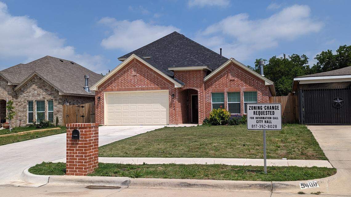 A single story brick house with metal sign on the lawn that reads, "zoning change requested."