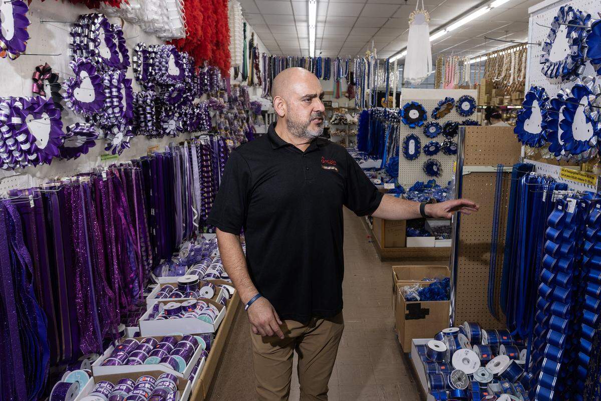 Mario Osuna walks down an aisle of a store with purple and blue ribbons and party supplies on either side of him.