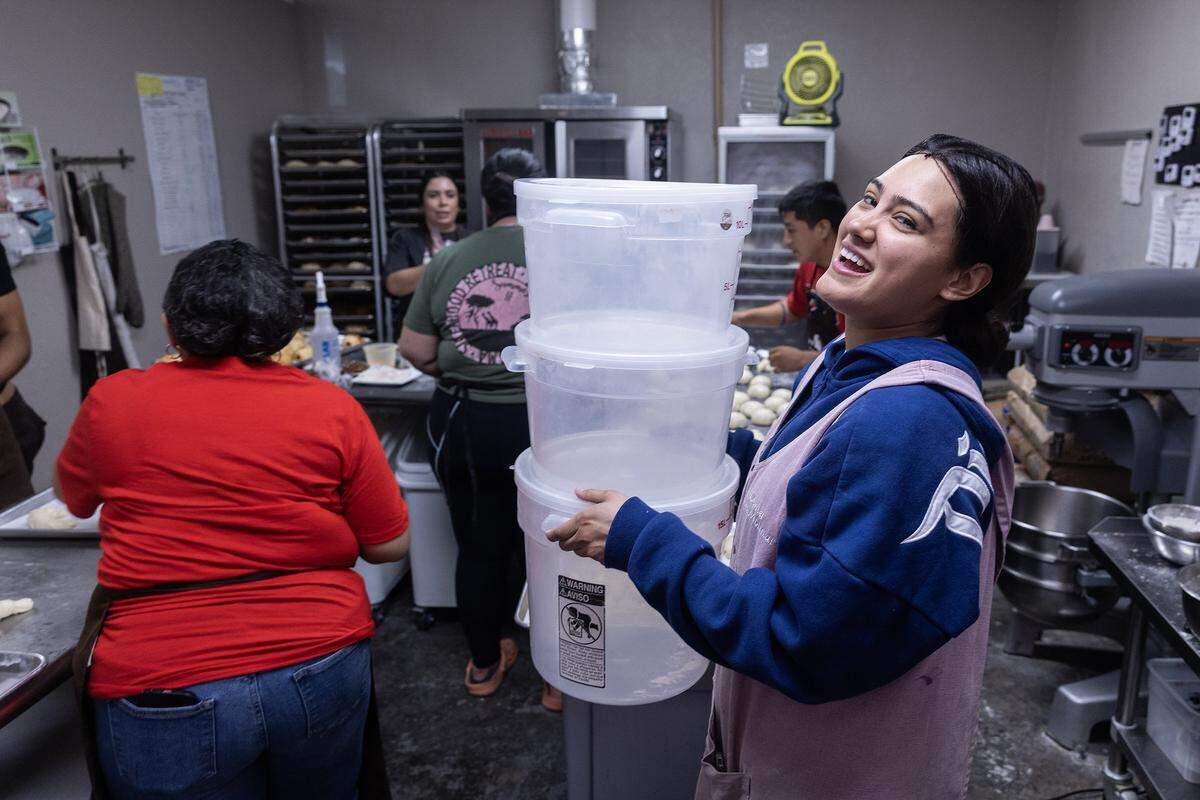 Laurita Molinar laughs while carrying plastic buckets through the bakery kitchen.