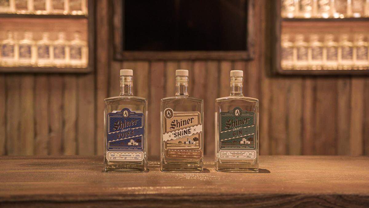Three bottles of spirits made by Shiner sit on a counter. There's vodka, shine and gin.