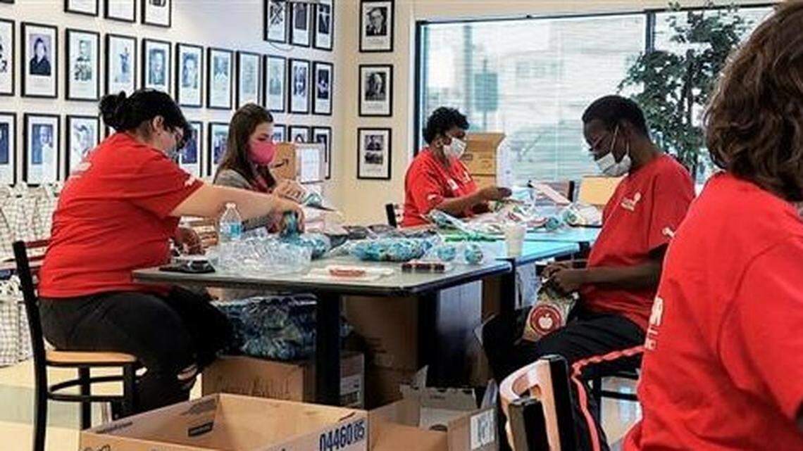Volunteers sit at a conference table and assemble goodie bags for students.