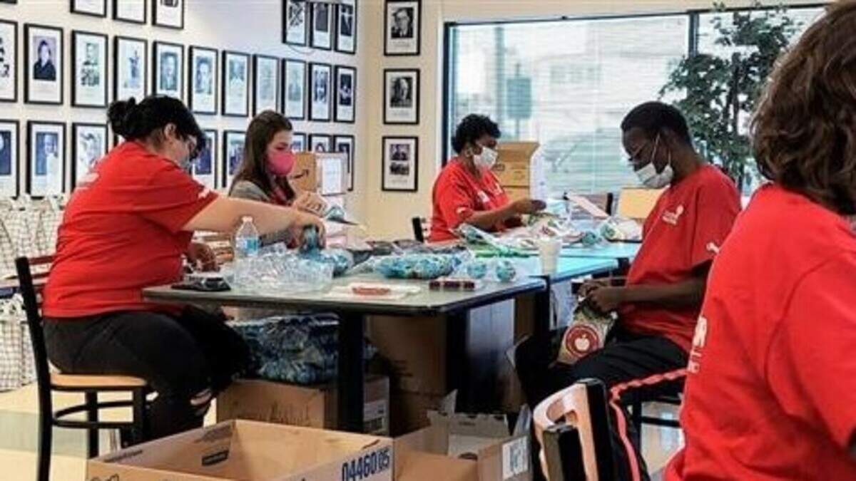 Volunteers sit at a conference table and assemble goodie bags for students.