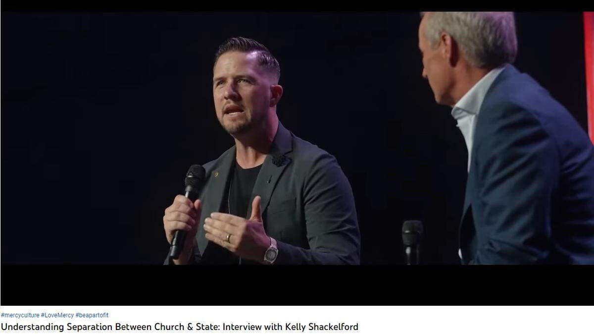 A white dude with a crew cut and a goatee talking into a microphone