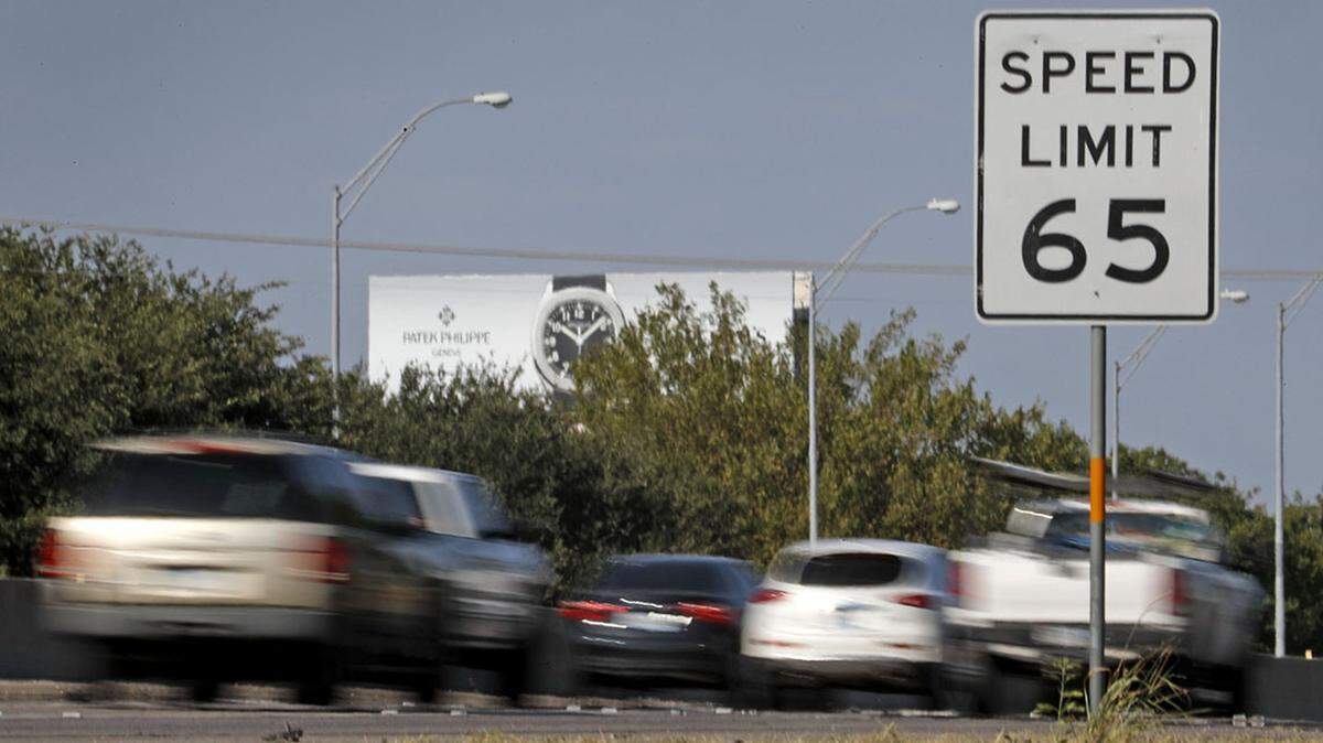 Cars moving down a highway with a speed limit sign for 65 on the side of the road.