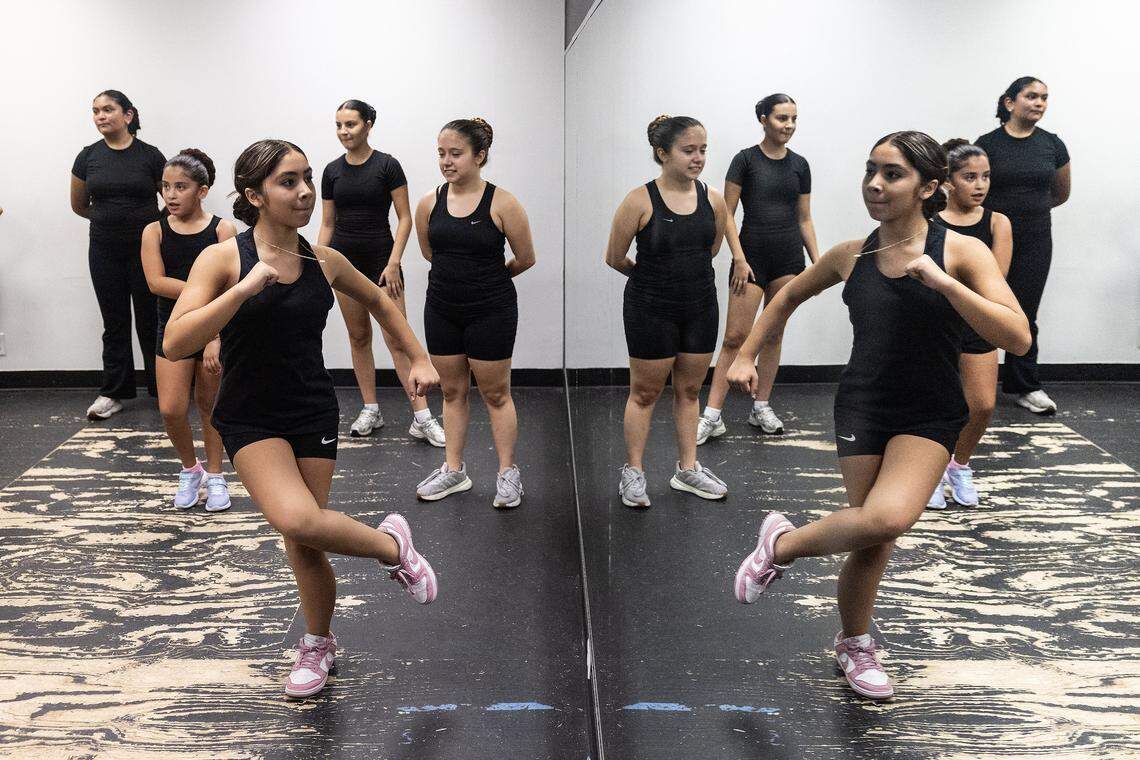 Leya Aguillon, 12, practices a one-legged spin while in front of the mirror of the dance studio while other dancers watch behind her. The wood of the floor is scuffed from use