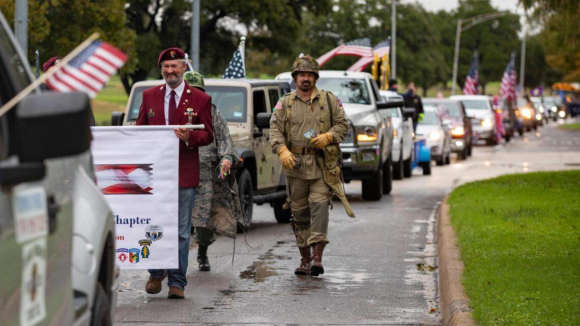 A line of dozens of vehicles and hundreds of people trickle through the street.