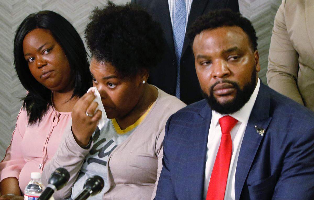 Amber Carr, center, wipes a tear as her sister, Ashley Carr, left, and attorney Lee Merritt, right, listen to their brother Adarius Carr talk about their sister Atatiana Jefferson during a news conference Monday, Oct. 14, 2019 in downtown Dallas. The family of the 28-year-old black woman who was shot and killed by a white police officer in her Fort Worth home as she played video games with her 8-year-old nephew expressed outrage that the officer had not yet been arrested or fired. (Irwin Thompson/The Dallas Morning News via AP)